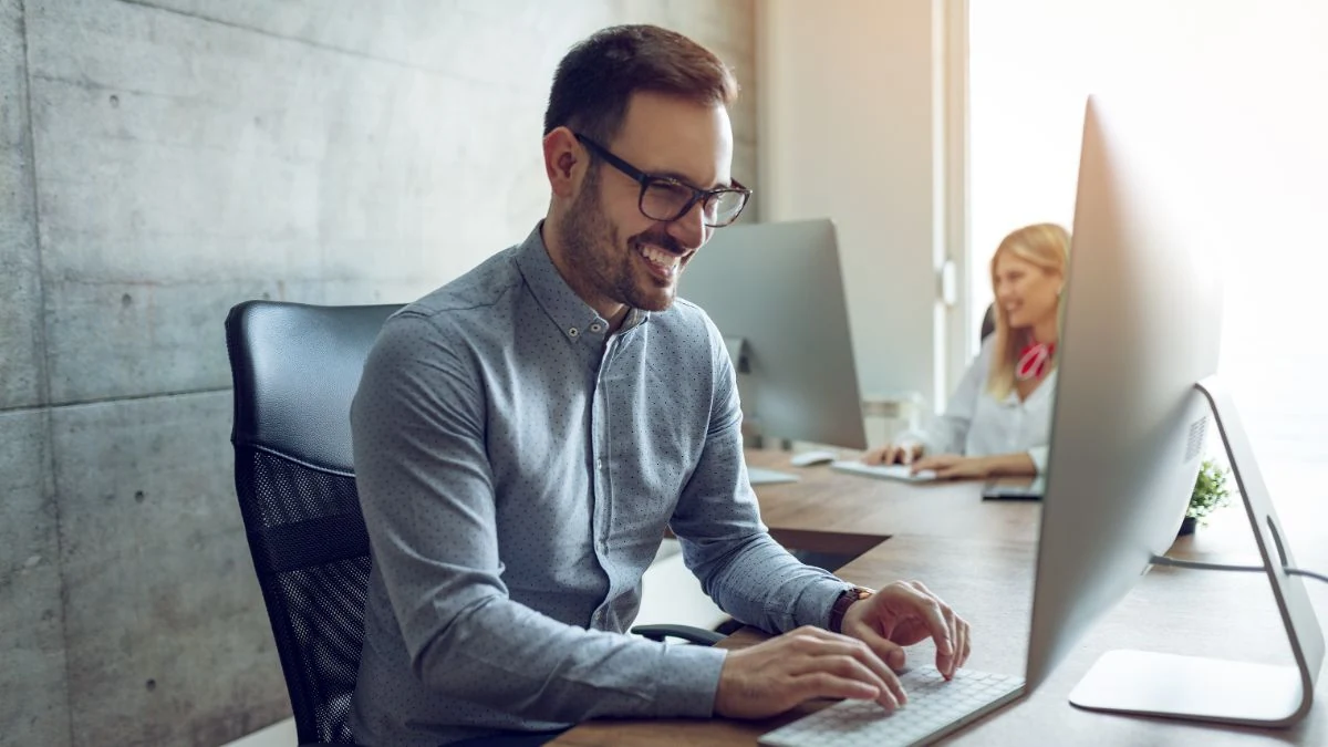Smiling sales manager in glasses typing at his desk