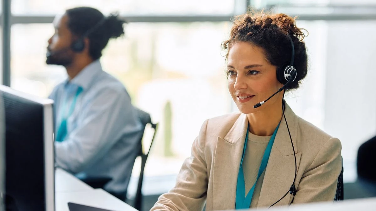 Agent in a beige blazer and headset listening to a client at her workstation