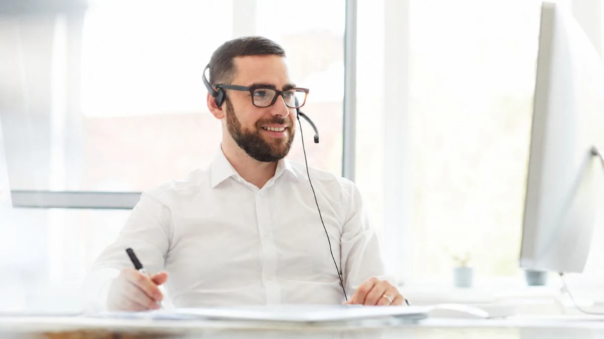 Sales rep in glasses taking notes during a discovery call on a headset