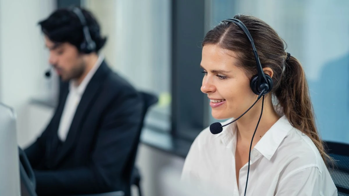 Two agents on headsets working side by side, a new hire smiling on a call in the foreground