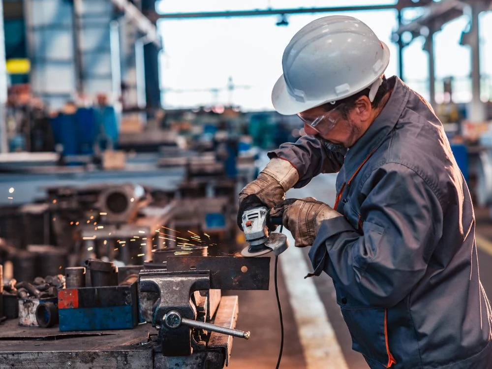 A manufacturing technician grinding a metal component at a workbench